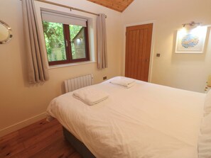 Ein Schlafzimmer mit einem Bett, einem Fenster mit Vorhängen, einem Heizkörper, einer Holztür und einer Wandleuchte.
