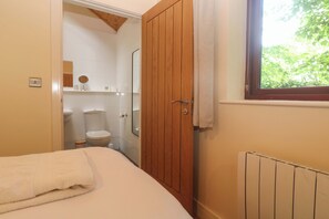 Ein Schlafzimmer mit Bett, Holztür, Fenster und Blick ins Badezimmer.