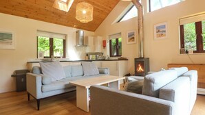 A modern interior with a wooden ceiling, a sofa, a table, and a fireplace. - The Lodge at Lamburn (Truro)