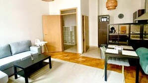 Ein Wohnzimmer mit einer Couch, einem Couchtisch und einem Essbereich mit Tisch und Stühlen. Es gibt eine Küchenzeile mit Schränken und einem Kühlschrank.