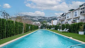 Una piscina con lettini, circondata da siepi curate e con montagne sullo sfondo.