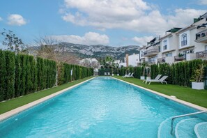 Ein Swimmingpool mit Liegestühlen, umgeben von ordentlich geschnittenen Hecken und einer Bergkulisse.