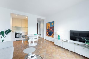 Ein modernes Wohnzimmer mit Fernseher, einem Essbereich und einer Küche im Hintergrund.