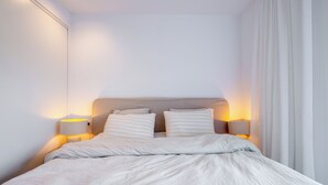 Un letto rifatto con cura, una testiera, due lampade da comodino e una finestra con tende.