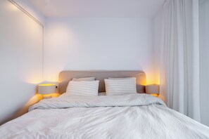Ein ordentlich bezogenes Bett mit Kopfteil, zwei Nachttischlampen und einem mit Vorhängen versehenen Fenster.