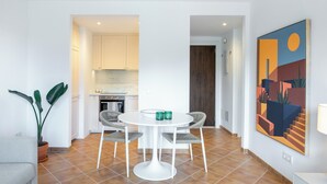 Una cucina moderna con mobili bianchi, un'area pranzo con un tavolo rotondo e due sedie, e un grande quadro astratto appeso al muro.