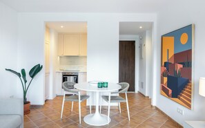 Eine moderne Küche mit weißen Schränken, einem Essbereich mit rundem Tisch und zwei Stühlen, und einem großen abstrakten Gemälde an der Wand.