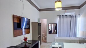 A hotel room with a bed, a desk, a chair, a TV, a mirror, and a hanging light fixture. - ITER HOTEL  (Rifaina)