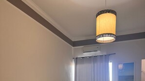 A hotel room with two beds, a large window with curtains, a ceiling light fixture, and a wall-mounted air conditioning unit. - ITER HOTEL  (Rifaina)