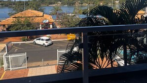 A view from a balcony overlooking a parking lot with a white car, a building with a red roof, and a body of water with hills in the background. - ITER HOTEL  (Rifaina)