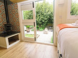 Ein Zimmer mit Holzboden, einem Bett mit orangefarbener Decke, einer weißen Tür zu einem Garten und einem Kamin.