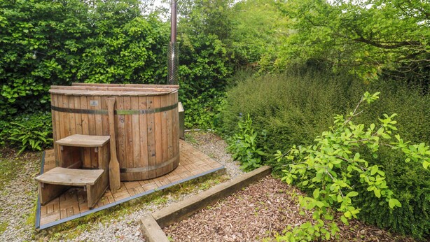 A wooden outdoor sauna structure with a bench, surrounded by dense greenery. - Shepherds Hut (Truro)