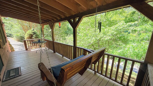 A wooden deck with a swing, a bench, and a view of a forest.
