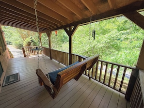 Une terrasse en bois avec une balançoire, un banc et une vue sur une forêt.