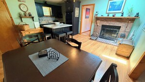 A dining area with a dark wooden table, chairs, and a kitchen in the background.