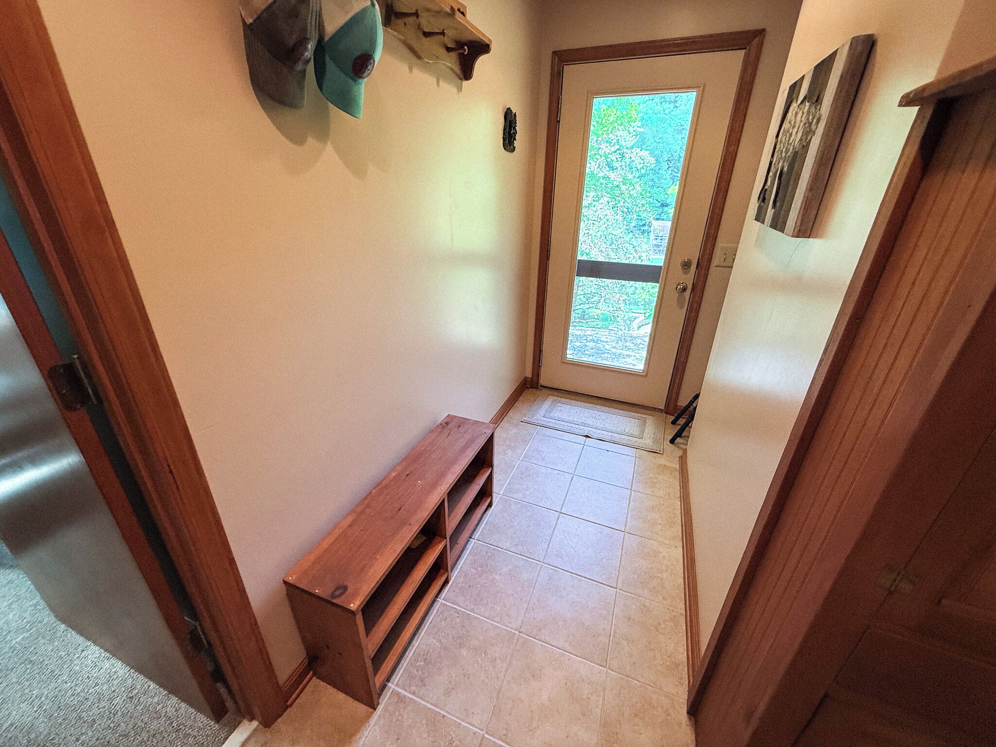 A hallway with a bench, a door with a view, and a small shelf with a decorative item.