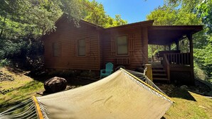 A wooden cabin with a porch, a hammock, and a chair.