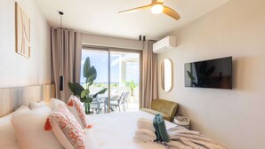 Une chambre d’hôtel équipée d’un lit, d’une télévision, d’un ventilateur de plafond, d’un balcon avec une table et des chaises, et d’un appareil de climatisation.