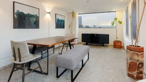 Zona pranzo moderna con tavolo in legno, una panca e vista sulla città attraverso ampie finestre.