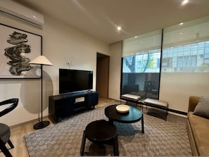 Ein modernes Wohnzimmer mit Flachbildfernseher, einer Couch, einem Couchtisch und einem großen Fenster mit Blick auf die Stadt.