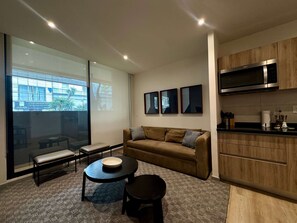 Ein modernes Wohnzimmer mit einer Couch, einem Couchtisch, einer Bank und einer Küchenzeile mit einer Mikrowelle.