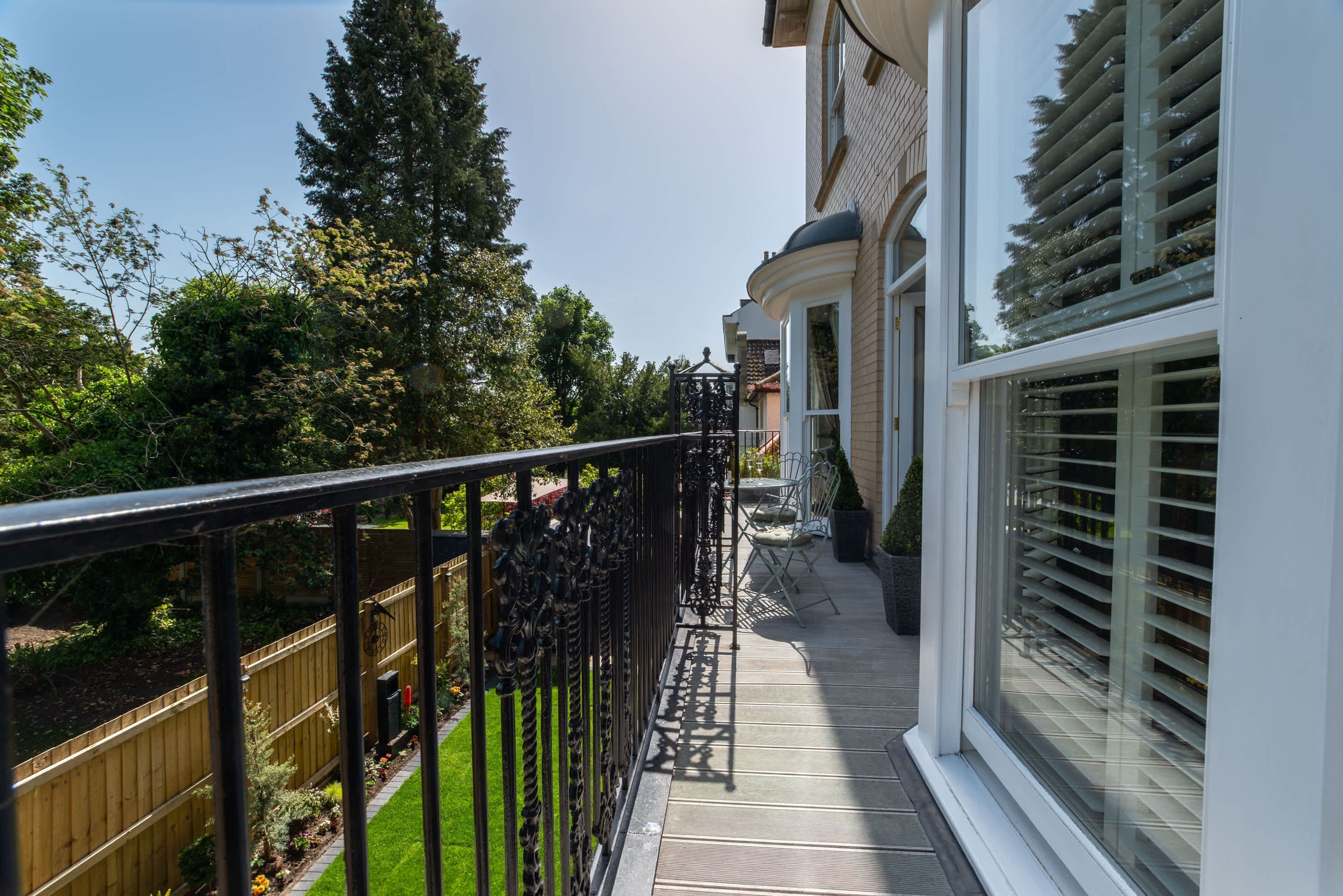 A balcony with a wooden fence, a metal railing, and a view of a garden and trees.