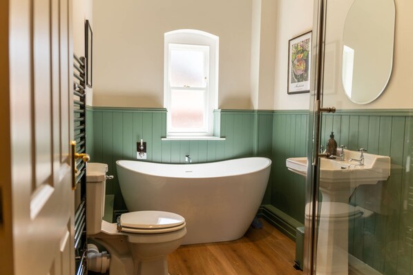 Ein Badezimmer mit freistehender Badewanne, Toilette, Waschbecken und einem Fenster.