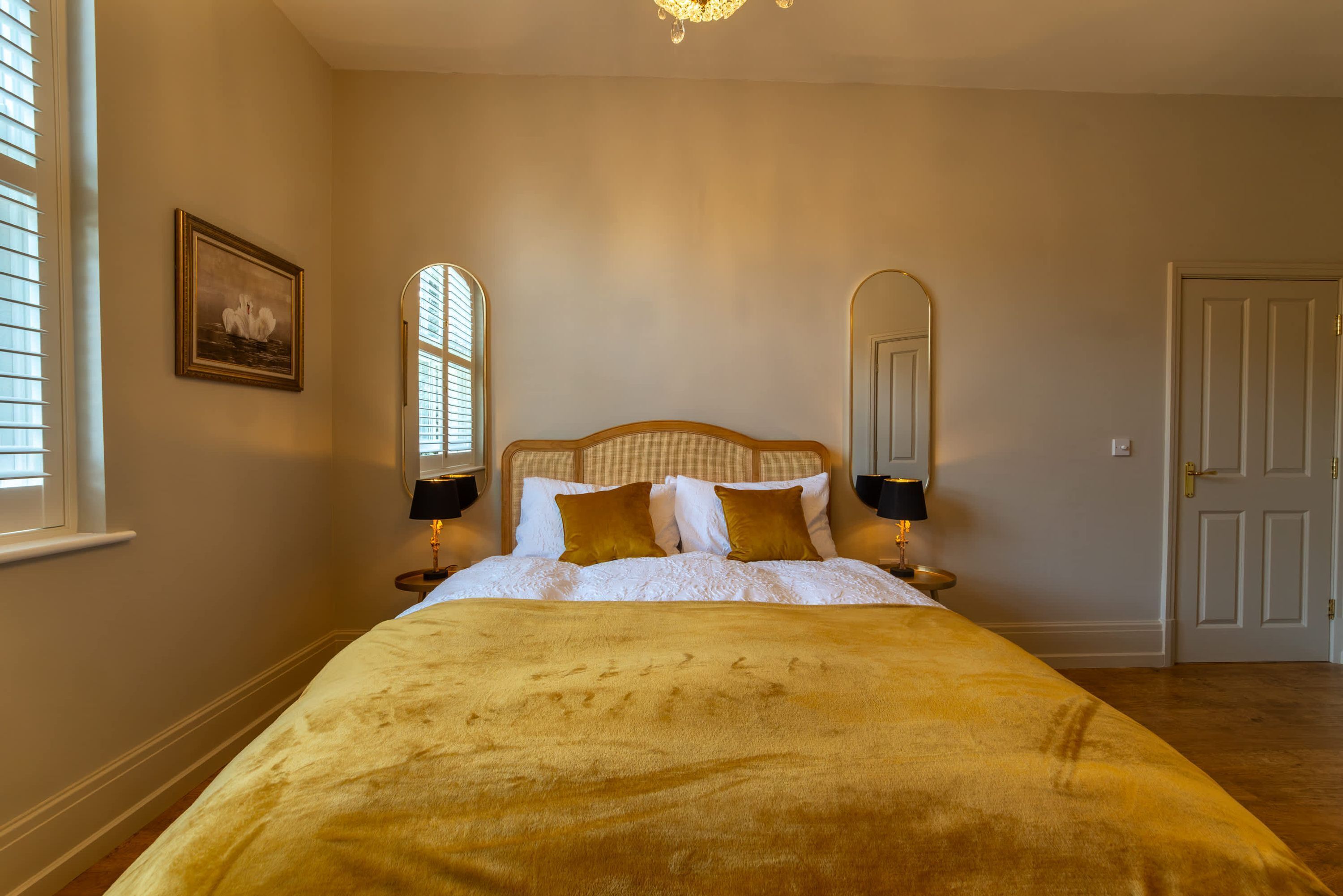 Quarto com cama grande, duas mesas de cabeceira, um candelabro e uma porta.