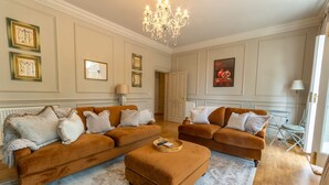 Uma sala de estar ampla com dois sofás marrons, um banquinho de madeira e um candelabro.