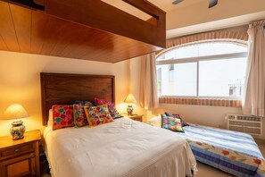 Ein Schlafzimmer mit einem großen Bett, zwei Nachttischen mit Lampen, einem Fenster mit Vorhängen und einem Holzbalken an der Decke.