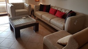 Een woonkamer met een beige bank, een fauteuil, een salontafel en een vloerlamp.