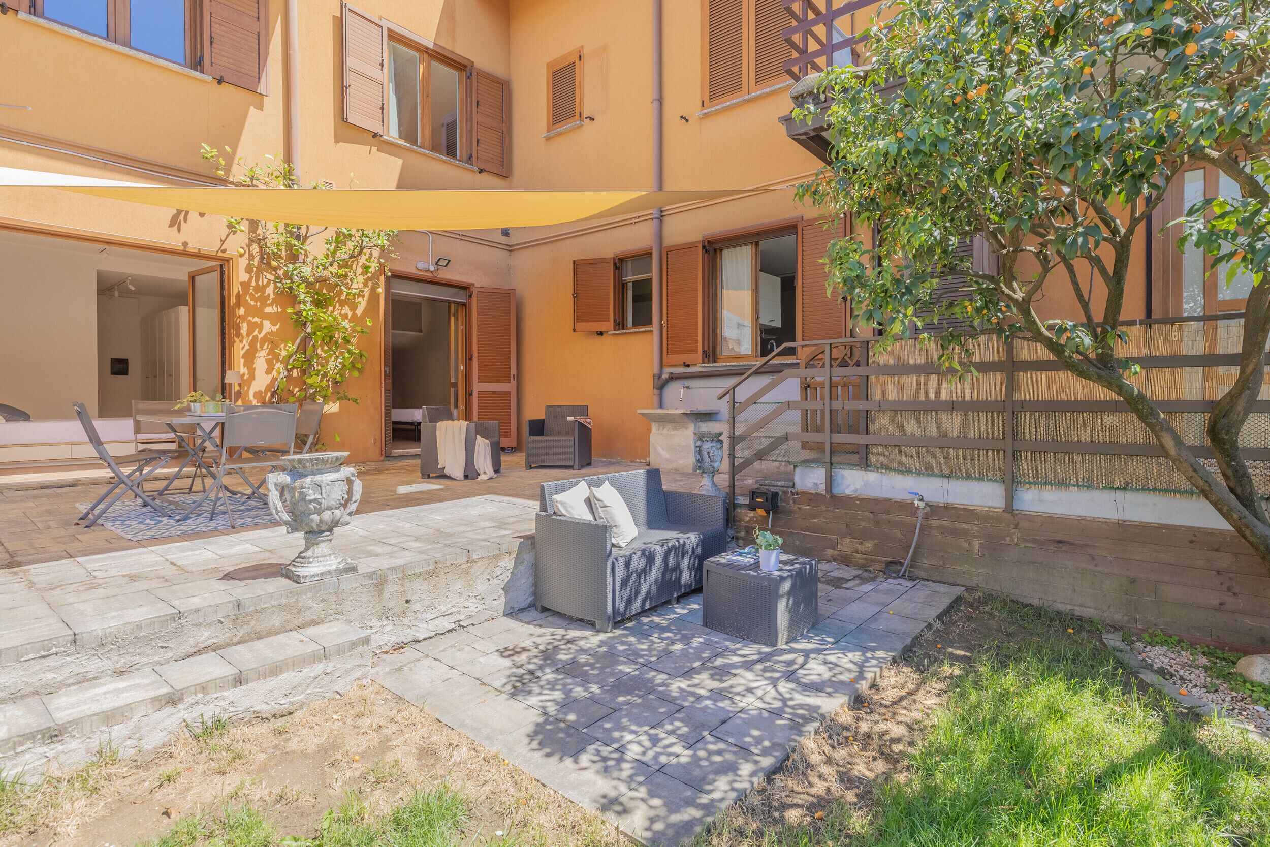 An outdoor patio with a sofa, chairs, and a table, a small tree, and a wooden fence.