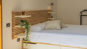 Uma cama com cabeceira de madeira, luminária de cabeceira e uma pequena estante com uma planta.