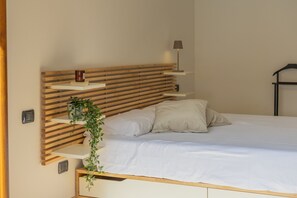 Uma cama com cabeceira de madeira, luminária de cabeceira e uma pequena estante com uma planta.