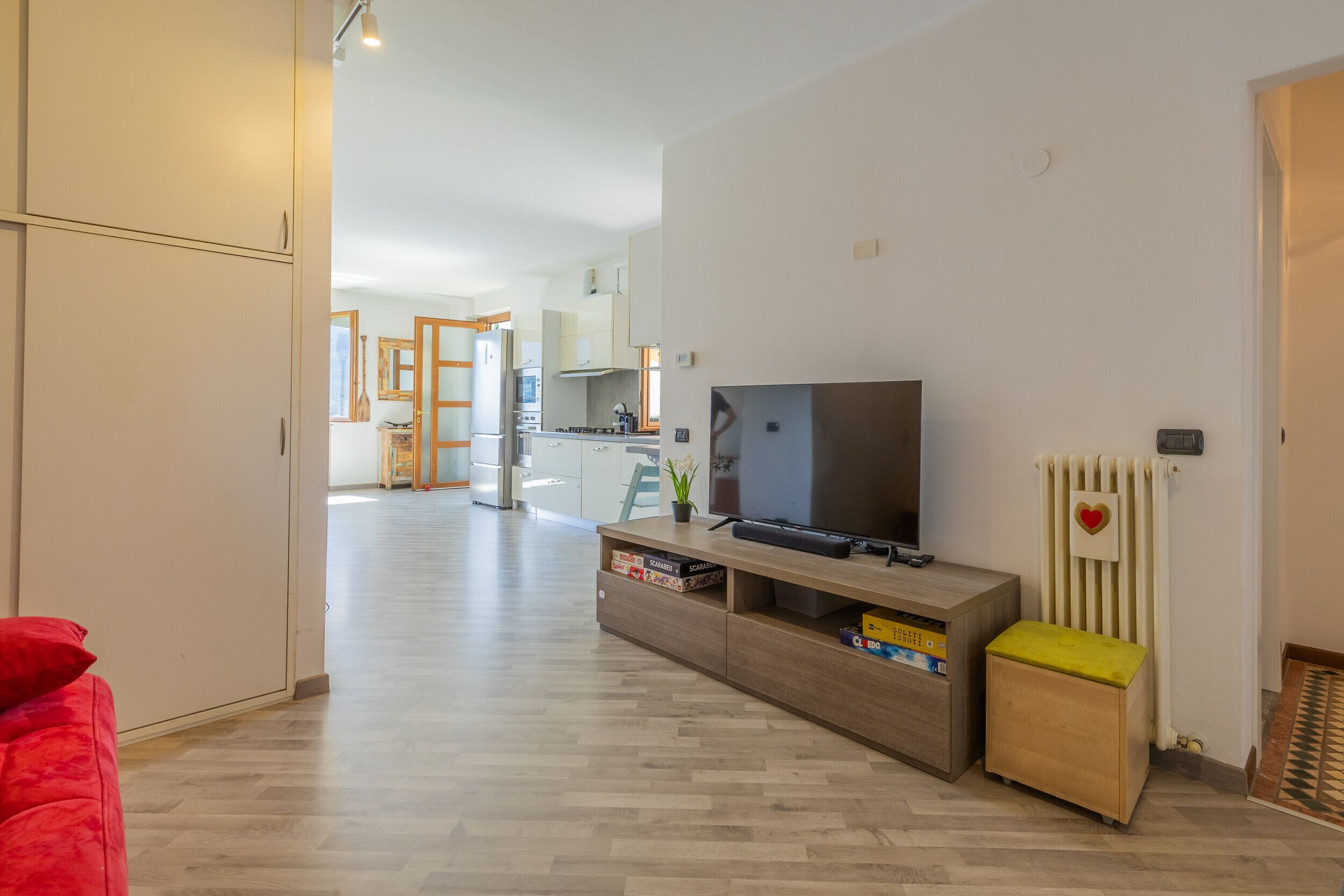 Un salon moderne avec un téléviseur à écran plat, un meuble de rangement en bois et un fauteuil rouge.