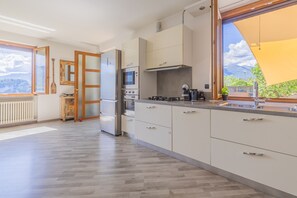 Ett modernt kök med vita skåp, rostfria vitvaror och ett stort fönster med utsikt över omgivningen.