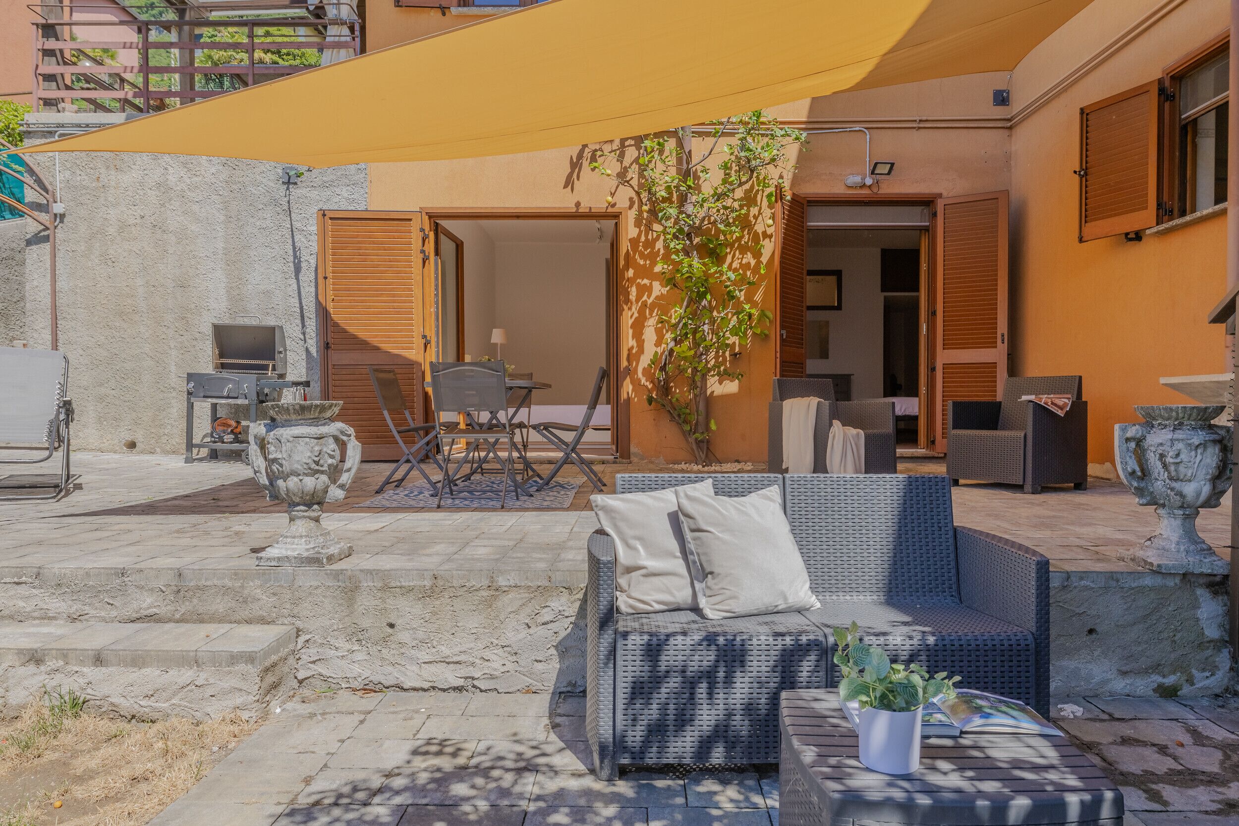 An outdoor patio with wicker furniture, a grill, and a potted plant.