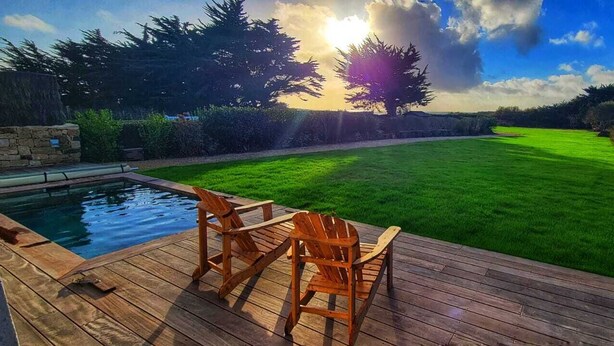 Eine Holzterrasse mit Stühlen, einem Schwimmbecken und einem gepflegten Rasen.