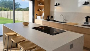Eine moderne Küche mit einer großen Kochinsel, Barhocker, einem Einbauofen und Blick ins Freie.