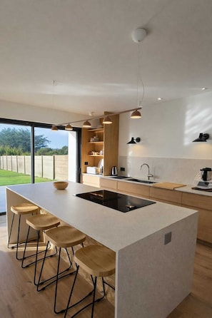 A modern kitchen with a large island, bar stools, a built-in oven, and a view of the outdoors. - Villa Côte Sauvage : quiet, swimming pool and sea view (Quiberon)