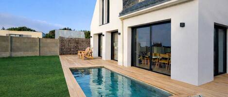 Een modern huis met een zwembad, een terras met stoelen en een stenen muur.