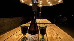 En flaska Cotillion Pinot Noir står på ett träbord tillsammans med två glas, under en ljusslinga som hänger som ett parasoll.