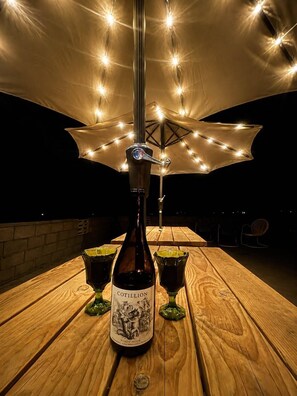 Eine Flasche Cotillion Pinot Noir auf einem Holztisch mit zwei Gläsern, unter einem Lichterbogen.