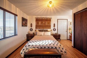 Ein Schlafzimmer mit Bett, Nachttischen, einer Bank, einem dekorativen Kopfteil, einer Wanddekoration und einer Tür.