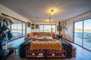 Ein großzügiges Wohnzimmer mit einer großen Couch, einem Couchtisch und einem Kamin. Mehrere Fenster sorgen für natürliches Licht und einen Blick ins Freie.