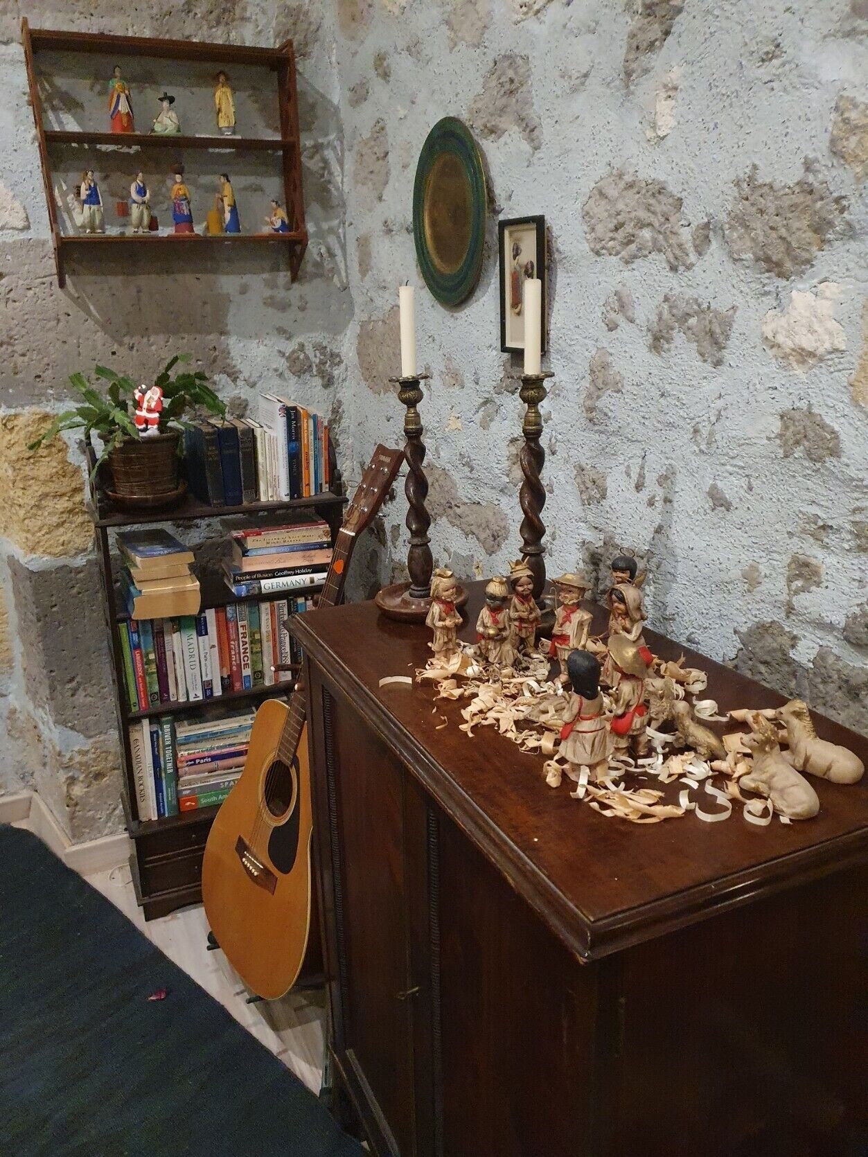 A room with a wooden cabinet, a bookshelf, a guitar, and a wall with a textured surface.