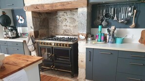 A kitchen with a vintage stove, wooden cabinets, and a stone wall. - Chambre Lavande aux Quatre Vents with Shared Terrace and Garden (Francescas)