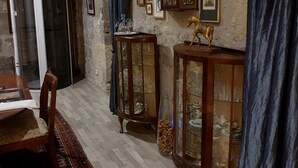 A room with a wooden dining table, chairs, a patterned rug, a glass cabinet with wine glasses, a blue curtain, and a wall with framed pictures. - Chambre Lavande aux Quatre Vents with Shared Terrace and Garden (Francescas)