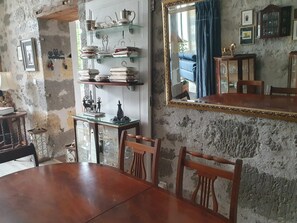 Uma área de refeições com mesa e cadeiras de madeira, uma prateleira de vidro com louças, um espelho e uma parede rústica.