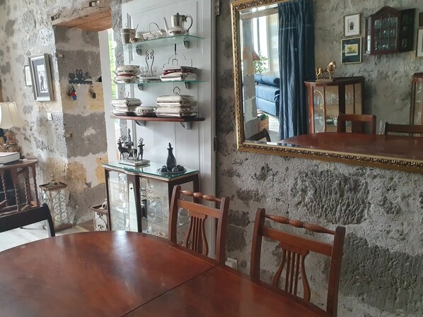 Un comedor con una mesa y sillas de madera, un estante de vidrio con vajilla, un espejo y una pared rústica.